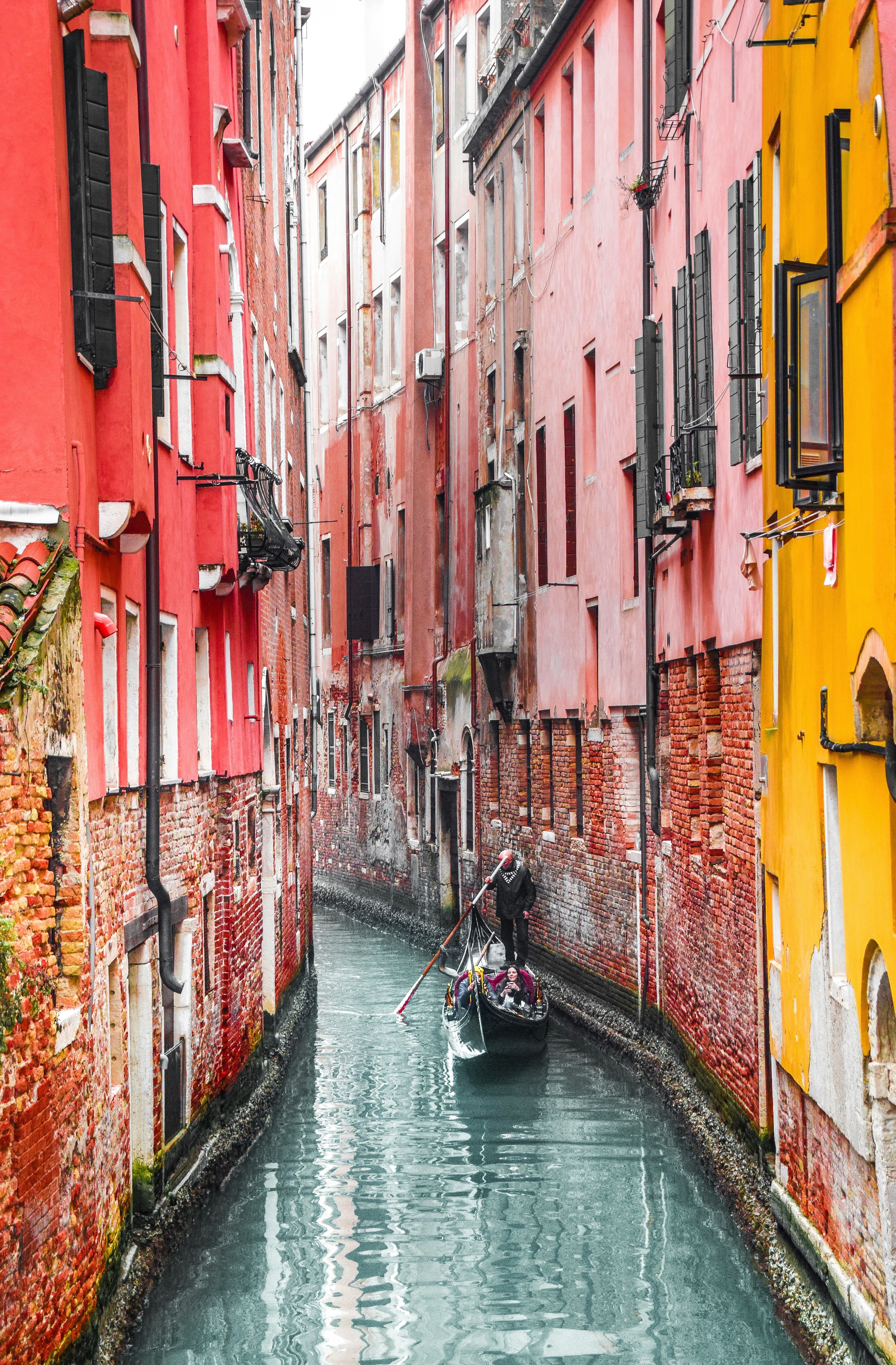 man in black jacket riding on boat on river between red and yellow concrete buildings during